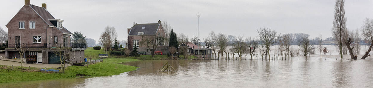 Huizen bij een overstroomde rivier. Het water komt bijna tot aan de woningen, die iets hoger liggen.