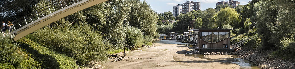 Een drooggevallen rivier heeft gevolgen voor het dagelijks leven. Woonboten liggen op de bodem, doordat er te weinig water is.