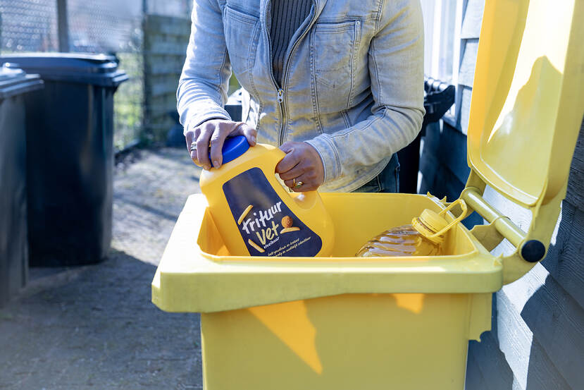 Een persoon levert een fles gebruikt frituurvet in in een inzamelcontainer.