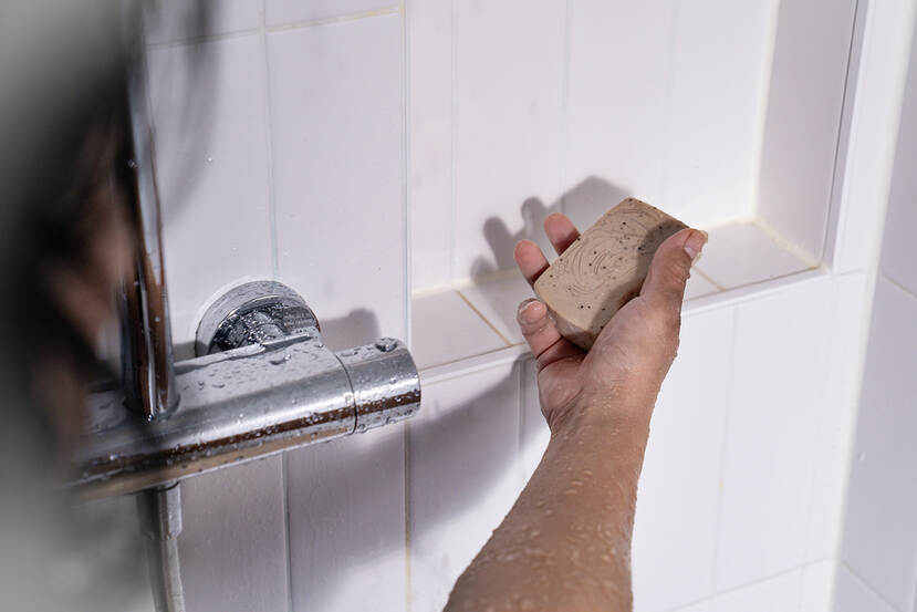 Een persoon gebruikt een shampoobar onder de douche.