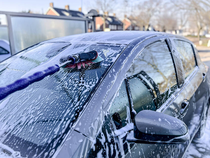 Een ingezeepte auto wordt met een bezem gewassen in een wasstraat.