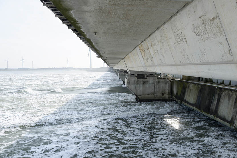 Close-up van de Oosterscheldekreing, één van de Deltawerken in Nederland. Links op de achtergrond staan windmolens op open water, rechts zien we de dichte schuiven van de kering die het water tegenhouden..