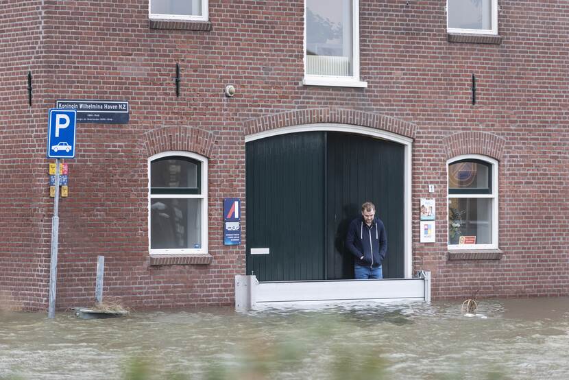 Een persoon staat achter een waterkerend schot bij de voordeur terwijl de straat is overstroomd.