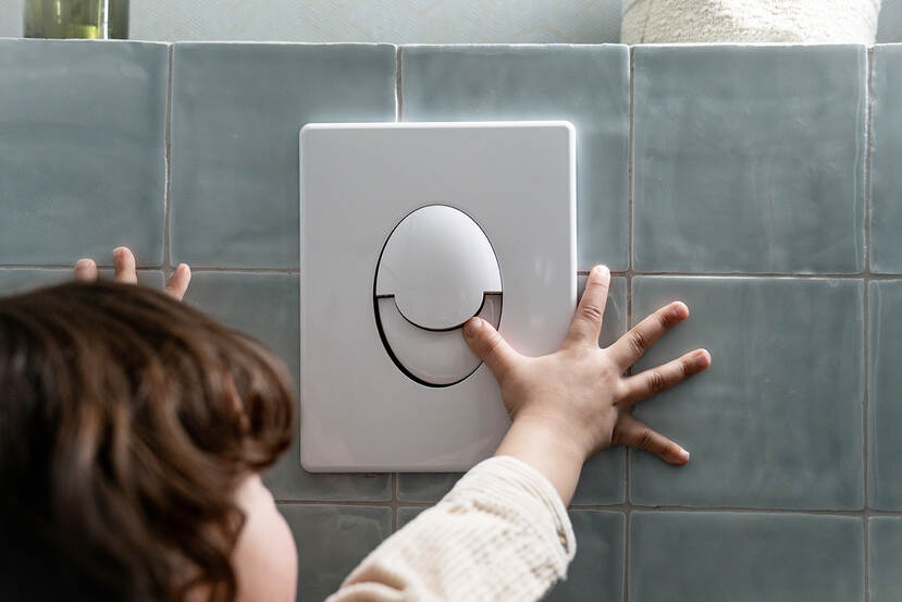 Een kind drukt op de kleine spoelknop van het toilet om water te besparen bij het doorspoelen.